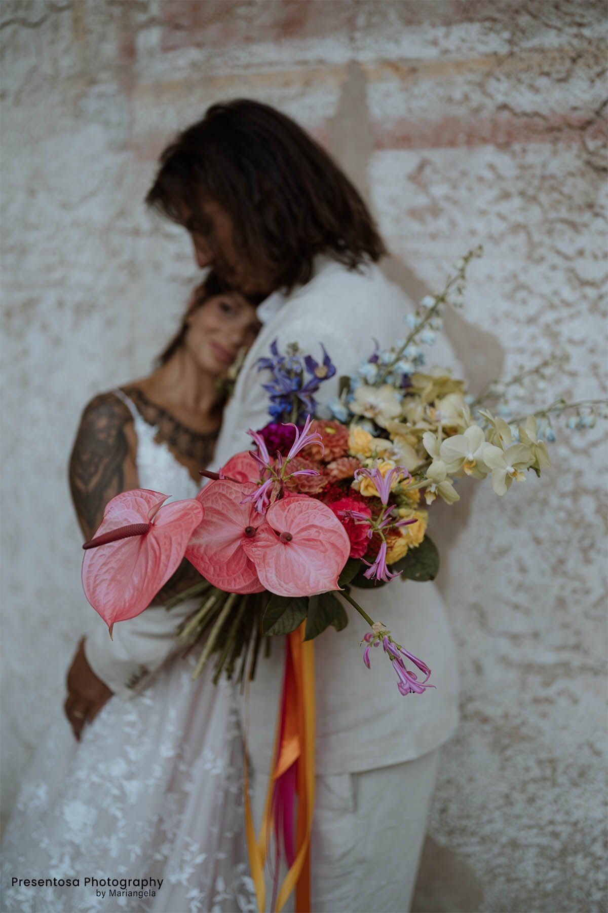 Sposi abbracciati con un bouquet di anthurium rosa e nastri colorati