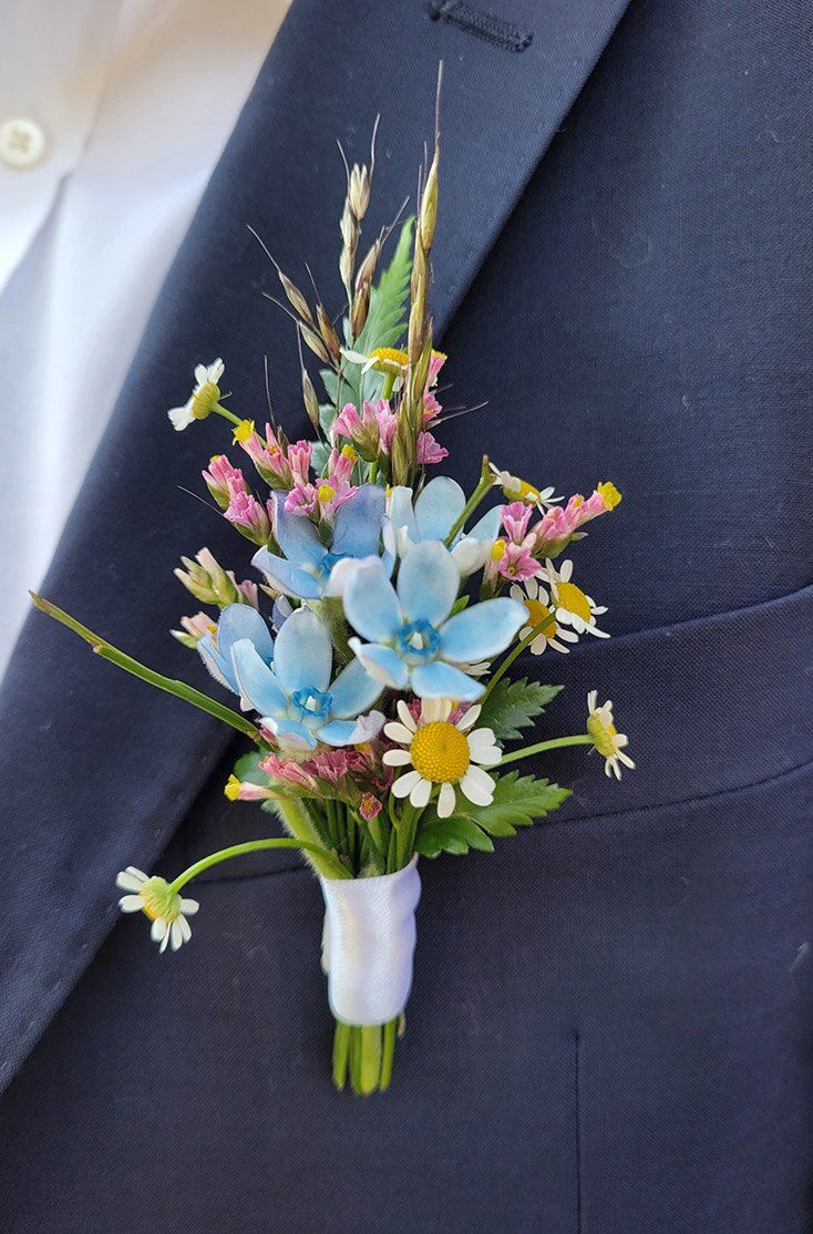 Boutonnière di fiori di campo azzurri e rosa sulla giacca dello sposo